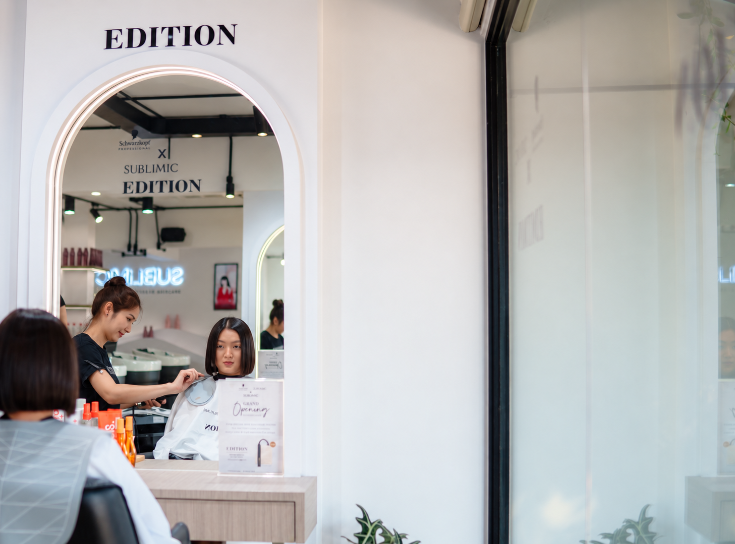 Stylist cutting a client's hair, seen in the arch mirror beneath the EDITION sign