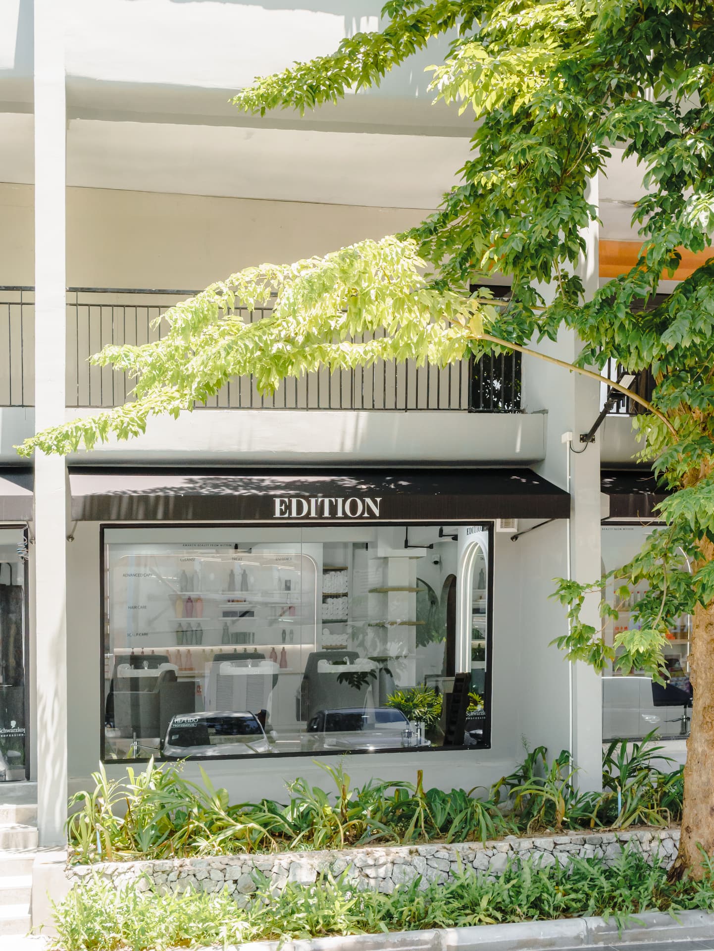 EDITION Salon shop window and awning framed by trees in the sunlight